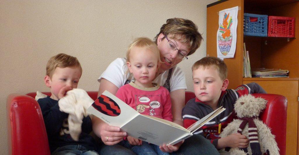 Een pedagogisch medewerker leest drie kinderen voor op de rode bank